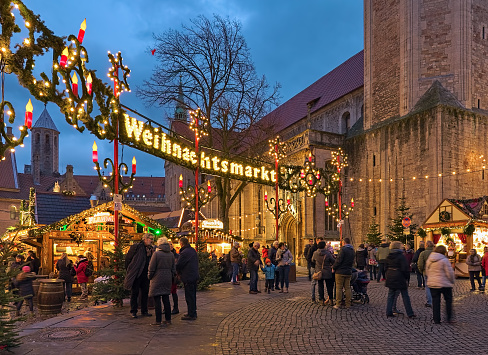 Braunschweig, Germany - December 7, 2018: Braunschweiger Weihnachtsmarkt - the Christmas market at Burgplatz square close to Brunswick Cathedral and medieval Castle Dankwarderode in twilight. The history of Braunschweig Christmas market goes back to the year 1505. Unknown people walk around the square.