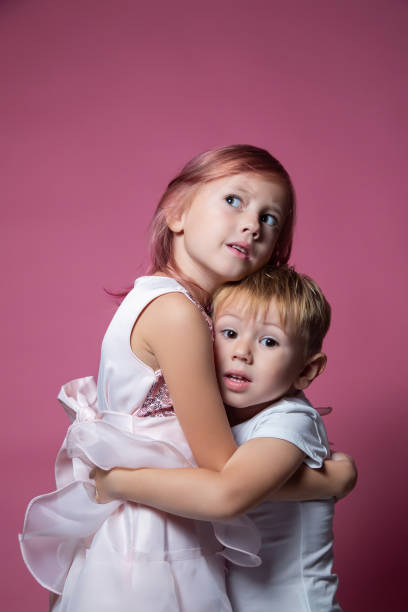 istock Caucasian brother and sister ,hugging on camera on pink background studio shot. 1343555469