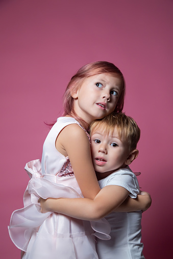 Caucasian brother and sister ,hugging on camera on pink background studio shot. Family ties, friendship, happy childhood concept.