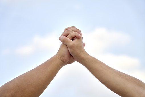 The interlocking fingers of two East Asian men's hands ， in front of the sky background