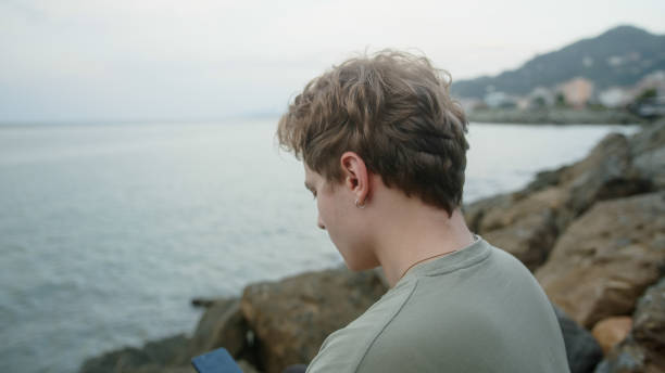 istock Handsome blond boy making phone call with smartphone by the sea 1343559411