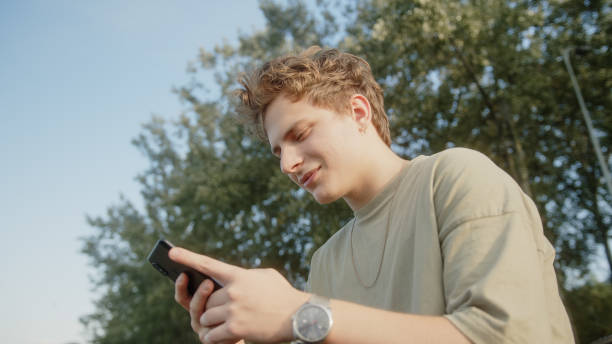 istock Handsome blond hair colored eyed boy while surfing the internet getting new message notification and answers with a smile. Beautiful nature and trees background.Anahtar sözcük di 1343559443