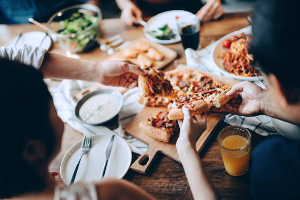 primo piano di un giovane gruppo di amici che passano e servono cibo mentre si divertono insieme. si divertono, chiacchierano e banchettano con cibo e bevande alla cena - pizza foto e immagini stock