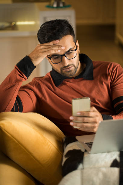 l'uomo si sente depresso nel ricevere cattive notizie usando il telefono - home interior young adult professional occupation vertical foto e immagini stock