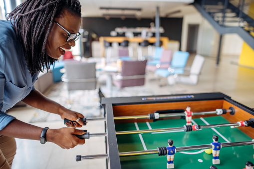 Diverse young coworkers playing table football on break in office.