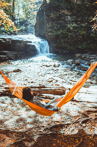 woman laying on hammock with view of autumn waterfall sunny warm day hiking concept