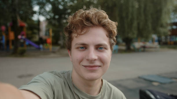 istock Young handsome boy with blond colored eyes is video calling or vlogging with the phone in his hand in a park outdoors 1343565551