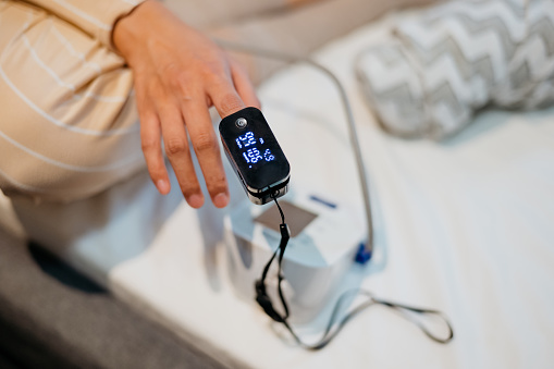 Close up of hand of an Asian woman measuring blood oxygen level with a pulse oximeter. Woman insert her index finger into pulse oximeter for SpO2 measurement.