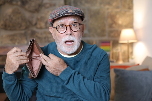 A senior man with financial problems is showing his empty wallet at home