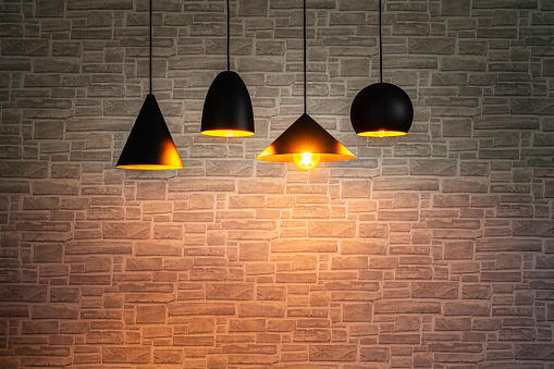 Low key shot of four black pendant electric lamps hanging against brick wall background. Copy space. High resolution 42Mp studio digital capture taken with SONY A7rII and Zeiss Batis 40mm F2.0 CF lens