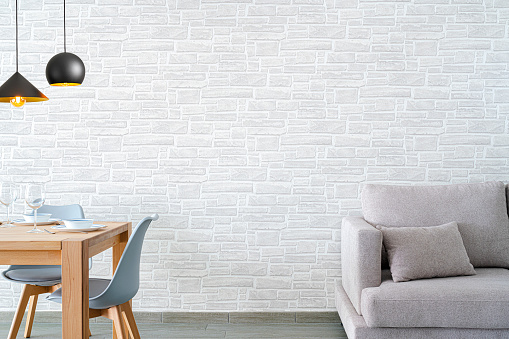 Gray sofa and wooden dining table with chairs shot against gray brick wall. High resolution 42Mp studio digital capture taken with SONY A7rII and Zeiss Batis 40mm F2.0 CF lens