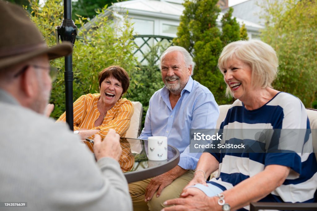 Friends Having a Laugh in the Garden Senior friends sitting in the garden on a summers day together. They are sitting and having a laugh over a cup of tea. Senior Adult Stock Photo