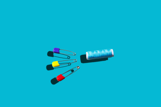 Three safety pins in front of sewing thread on blue background