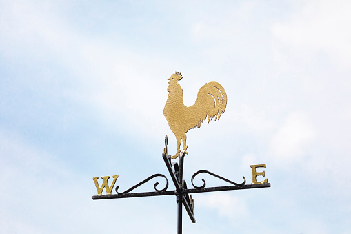 A low angle shot of a weathervane against a blue sky with clouds.