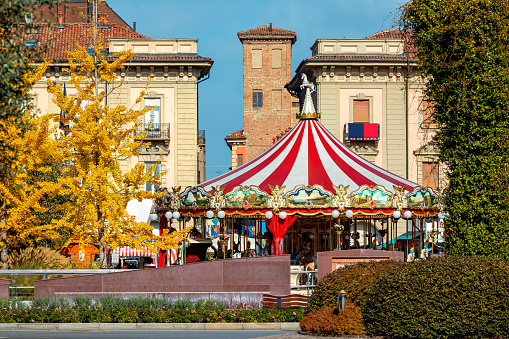 Carrousel on the town square among trees with yellow leaves in small town of Alba in Piedmont, Northern Italy.