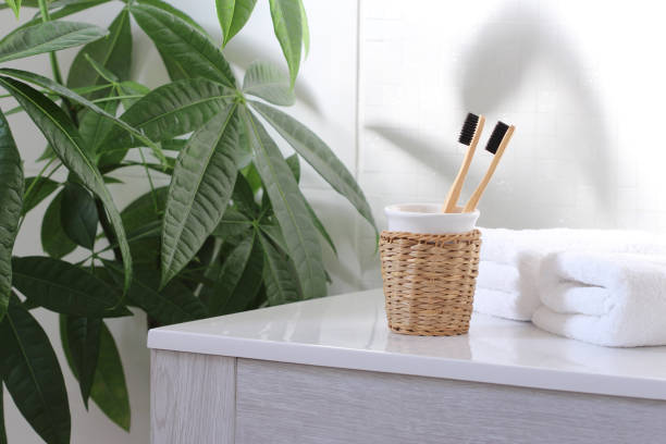 Natural toothbrushes  with charcoal for personal hygiene of eco-friendly people . Zero waste concept. Two bamboo toothbrushes with black bristles and charcoal on the bathroom sink next to a green plant and white towels. bathroom sink stock pictures, royalty-free photos & images