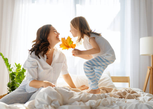 девочка и мама наслаждаются солнечным утром - waking up window women morning стоковые фото и изображения