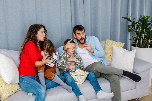 Family eating popcorn while watching tv at home