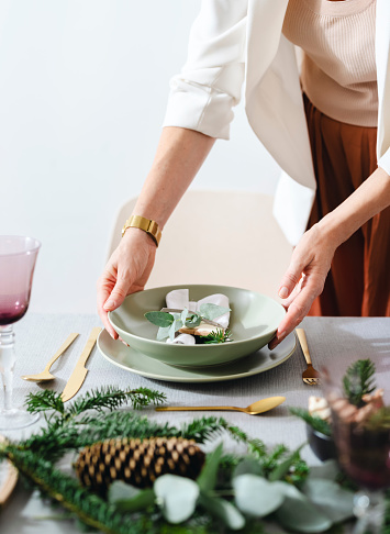 Unrecognizable female hands setting up Christmas table in dinning room.