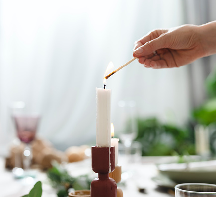 Unrecognizable female hands lights the candle on Christmas table in dinning room.