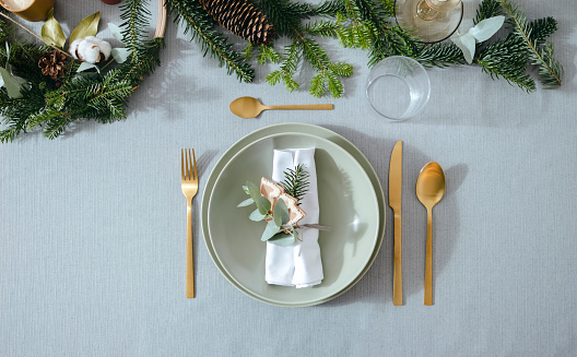 Flat lay of a holiday table setting with golden cutlery and green porcelain plate on a gray table.