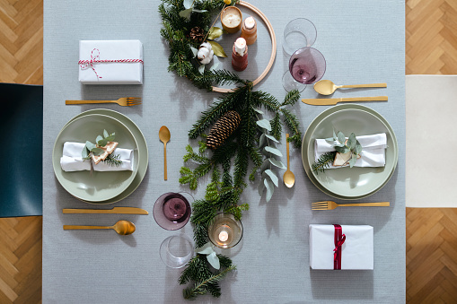 Beautiful holiday table setting with golden cutlery and green porcelain plate on a gray table with Christmas decoration and presents.