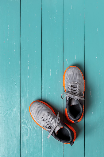 Pair of new gray textile sneakers over turquoise wooden floor. Modern laced up mesh fabric trainers with grooved orange sole for fitness, sport and active lifestyle. Vertical frame. Copy space. Top view.