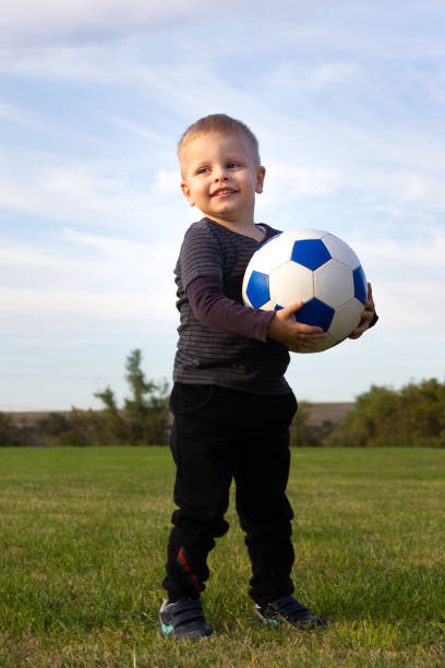 Portrait of a happy boy whit soccer ball and headphones standing outdoors and looking at camera