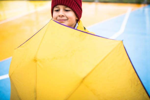 A cute boy is smiling behind an umbrella out on a rainy autumn day