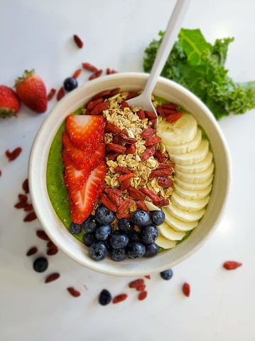 A smoothie bowl made of pineapple, banana, frozen yogurt, spinach and Kale. Topped with fresh banana, fresh strawberries, fresh blueberries, goji berries, granola and honey