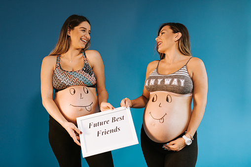 Two pregnant female friends with smiley face drawing on their pregnant bellies having fun