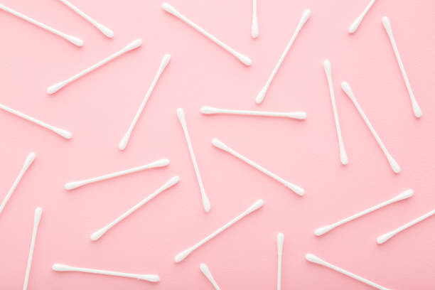 White sticks of cotton bud on light pink table. Pattern background. Pastel color. Closeup. Top down view.