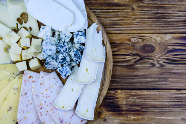 ломтики различных видов сыра на деревянном фоне. сырное блюдо - cheese tray cube swiss cheese стоковые фото и изображения