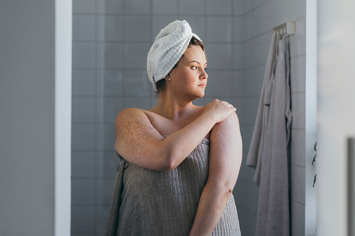 A young overweight woman applying body lotion after a shower in the morning