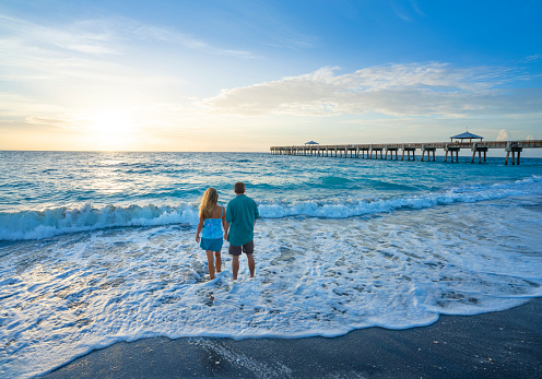 People walking on the beach. Summer beach scenery with pier in the background. Juno Beach, Florida, USA.