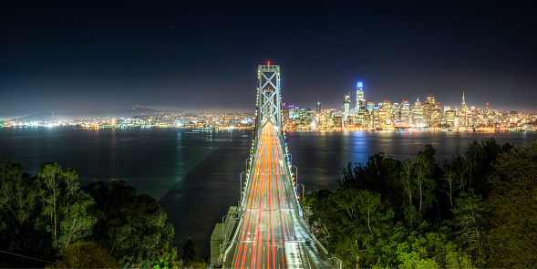 Car light trails over Oakland Bay Bridge with San Francisco skyline at night, California, USA