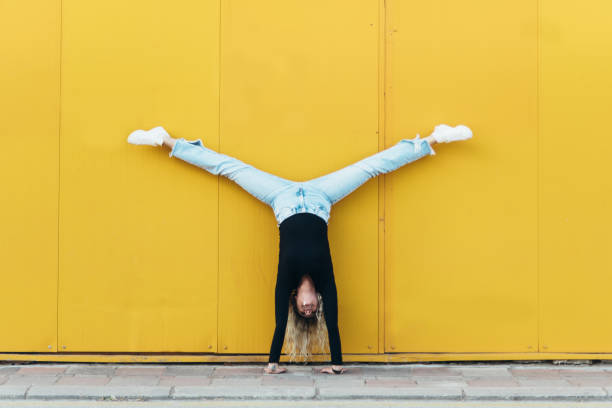 femme se tient debout devant le mur jaune - équilibre sur les mains photos et images de collection