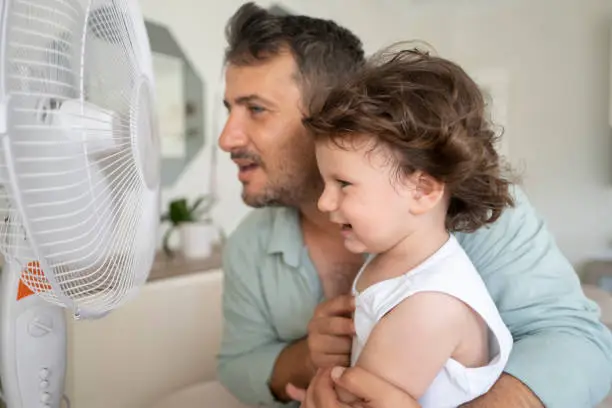 Photo of Father child is front of electric fan on hot summer day