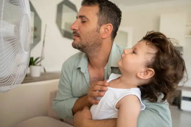 Photo of Father child is front of electric fan on hot summer day