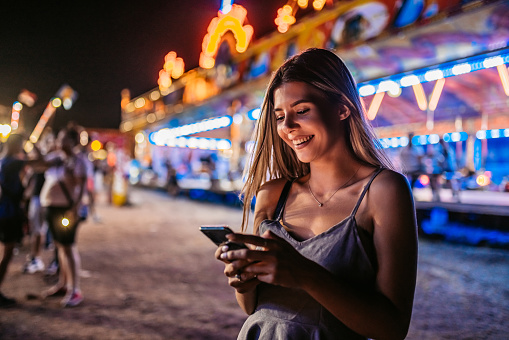 Young beautiful woman texting on her smartphone with fairy lights in the background.
