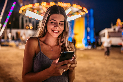 Young beautiful woman texting on her smartphone with fairy lights in the background.