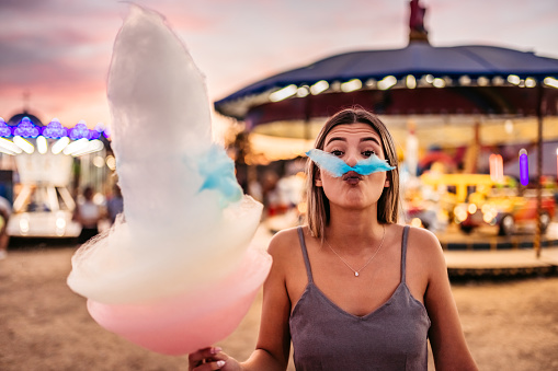 Funny moment of a beautiful woman making mustache of Colorful Candy at an Amusement Park.