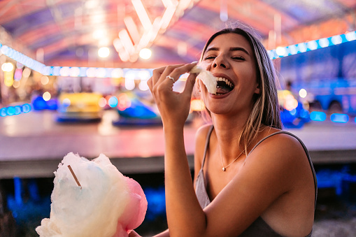 Funny moment of a beautiful woman eating Colorful cotton Candy at an Amusement Park.