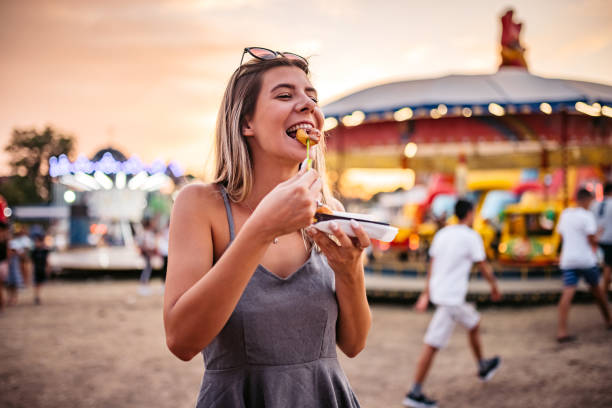 Cute Woman eating small donuts at the Funfair Funny moment of a beautiful woman eating small donuts at an Amusement Park. farmers market stock pictures, royalty-free photos & images