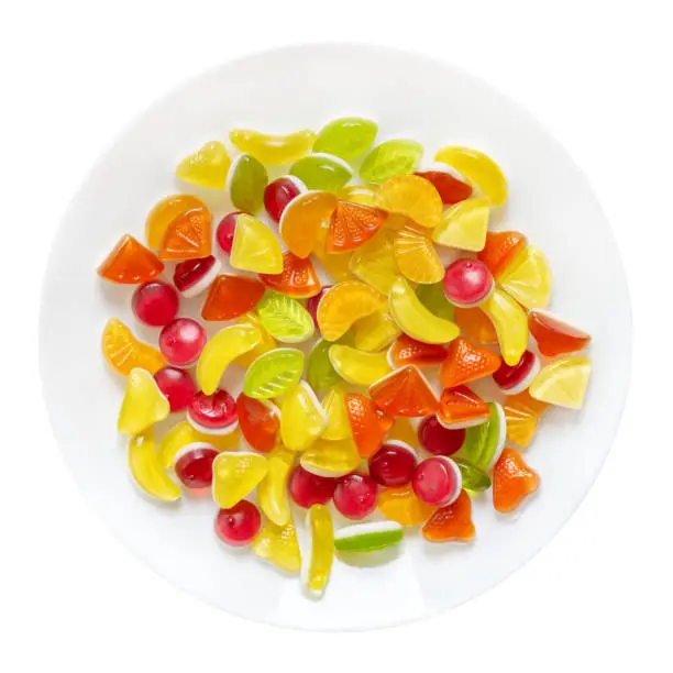 Photo of Gummy candies in the form of fruit slices on a plate isolated on a white background. Top view.