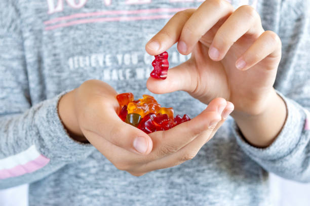 A girl holds a gummy bear in her hand, wants to eat jelly sweets. Close-up. Concept of children's delicacy, unhealthy food, vitamins for kids. A girl holds a gummy bear in her hand, wants to eat jelly sweets. Close-up. Concept of children's delicacy, unhealthy food, vitamins for kids. vitamin rich stock pictures, royalty-free photos & images