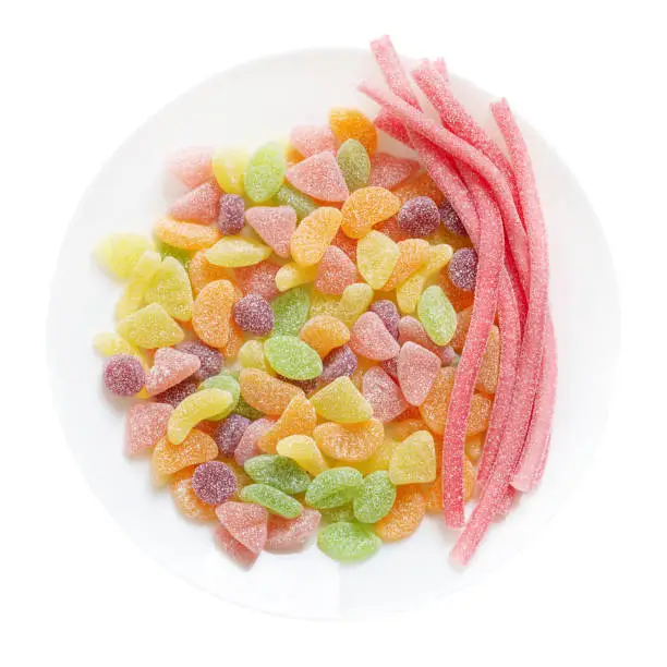 Photo of Gummy candies in the form of fruit slices, sticks in sugar on a plate, isolated on a white background. Top view.