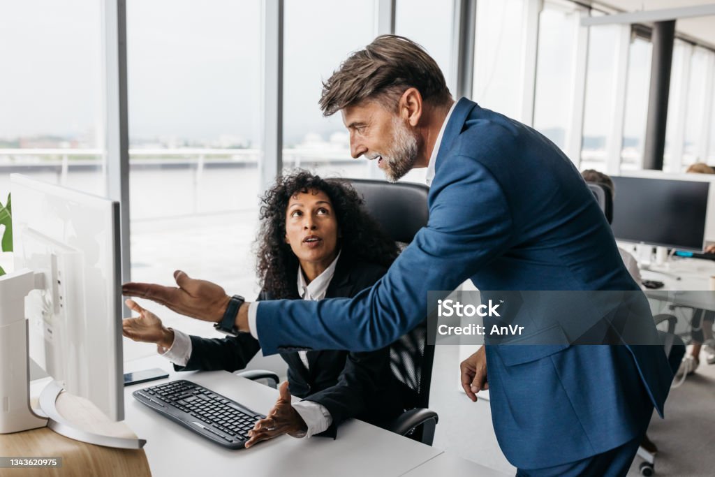 Business woman and businessman having a heated discussion A smartly dressed business woman and businessman are having a heated discussion. They are surprised by the results they received. The office they work in is bright with large windows and trendy furniture. Horizontal daylight indoor photo. Place of Work Stock Photo