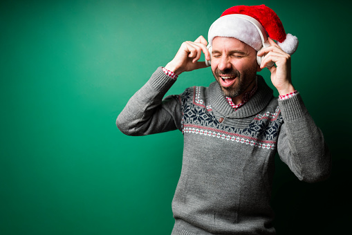 Having a great time. Excited young man in a christmas hat listening to happy music with wireless headphones