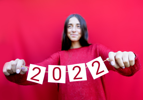 Teenager holding 2022 cards. Happy New Year celebration. Young girl and Christmas mood on red background